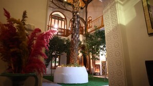 An indoor courtyard with a palm tree, a white planter, and a decorative wall. - Riad O-ly (Marrakech)
