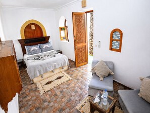A room with a bed, a sofa, a small table with a bottle, and a door with intricate woodwork. - Riad O-ly (Marrakech)