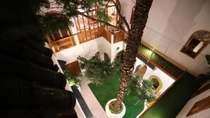 An indoor courtyard with a palm tree, a small garden, and a wooden balcony. - Riad O-ly (Marrakech)