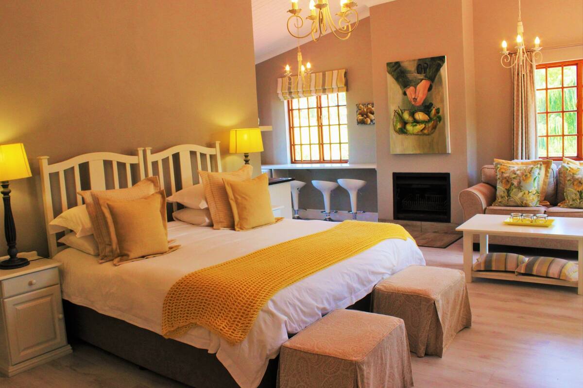 A bedroom with a large bed, bedside lamps, a fireplace, and a dining area with a table and chairs.