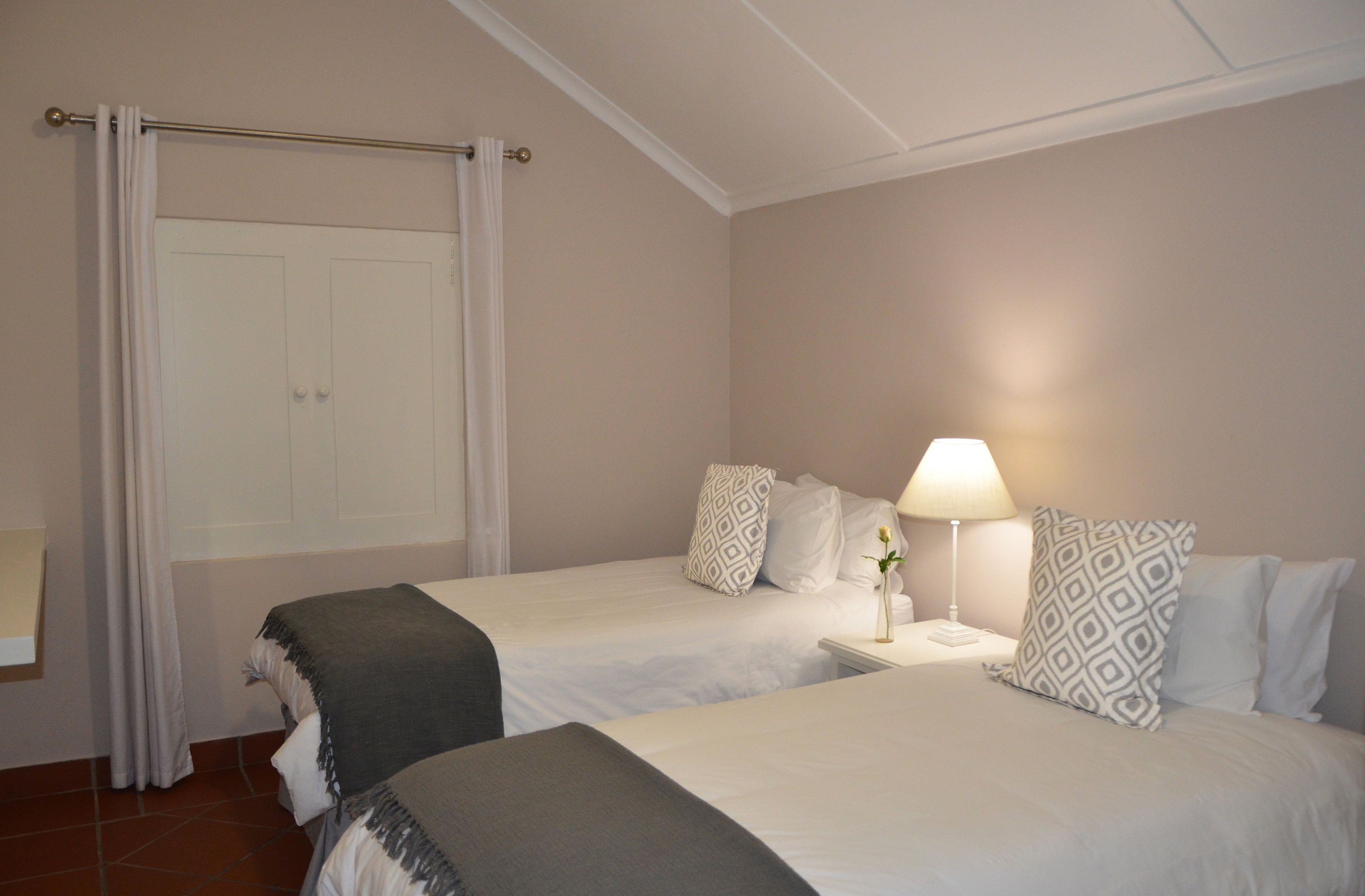 Een hotelkamer met twee bedden, een nachtkastje met een lamp, een witte deur en een gordijn.