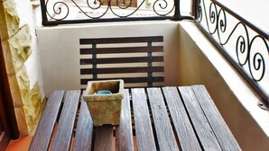 Un balcón con una mesa y banco de madera, un muro de piedra y vista a un parque.
