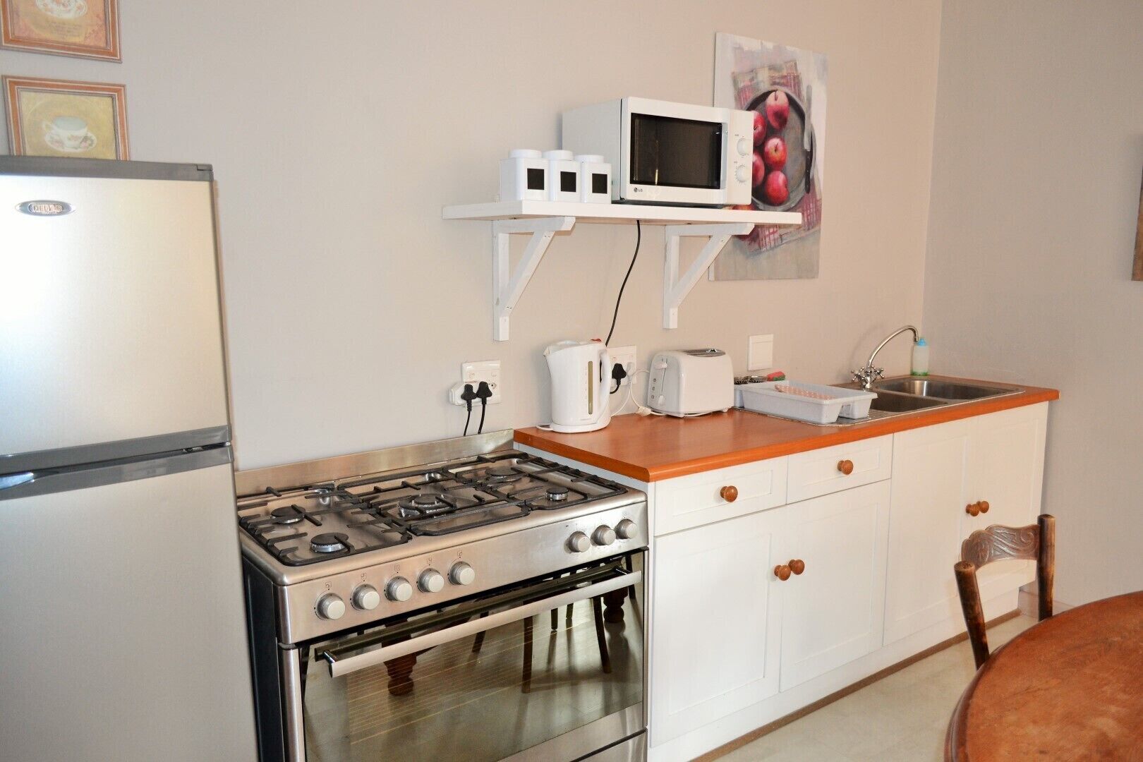 A compact kitchen with a gas stove, oven, white cabinets, a microwave on a shelf, and a sink.