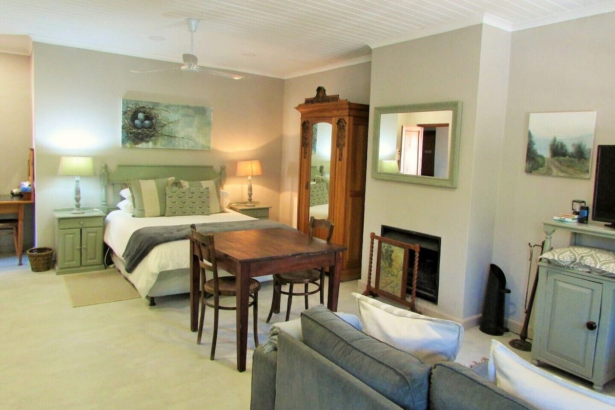 A bedroom with a bed, bedside tables, a dresser, a mirror, a fireplace, and a dining area with a table and chairs.