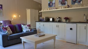 Una sala moderna con un sofá gris, una mesa de centro blanca y una cocina con armarios blancos, un tostador y una tetera.