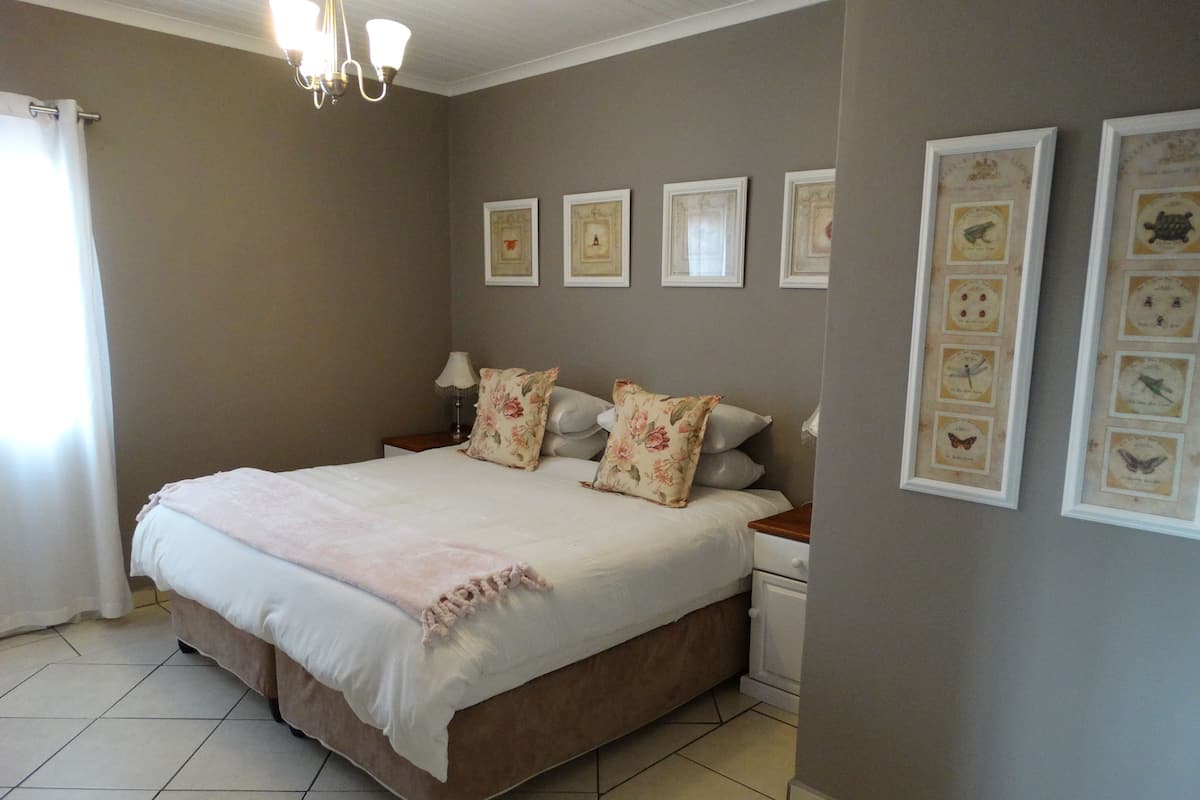 A bedroom with a large bed, a nightstand, a lamp, and framed pictures on the wall.