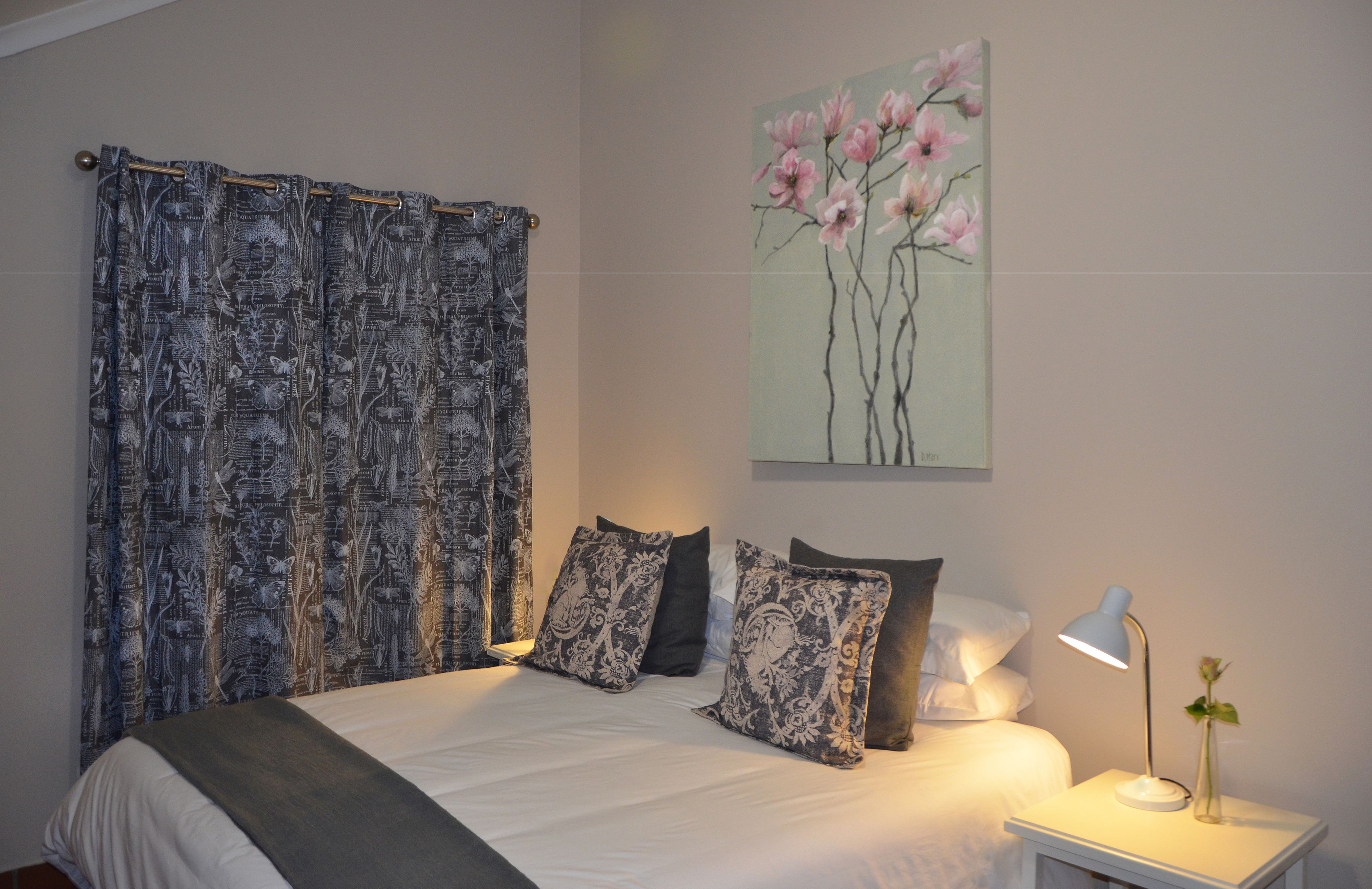 A bedroom with a bed, pillows, a nightstand, a lamp, and a painting on the wall.
