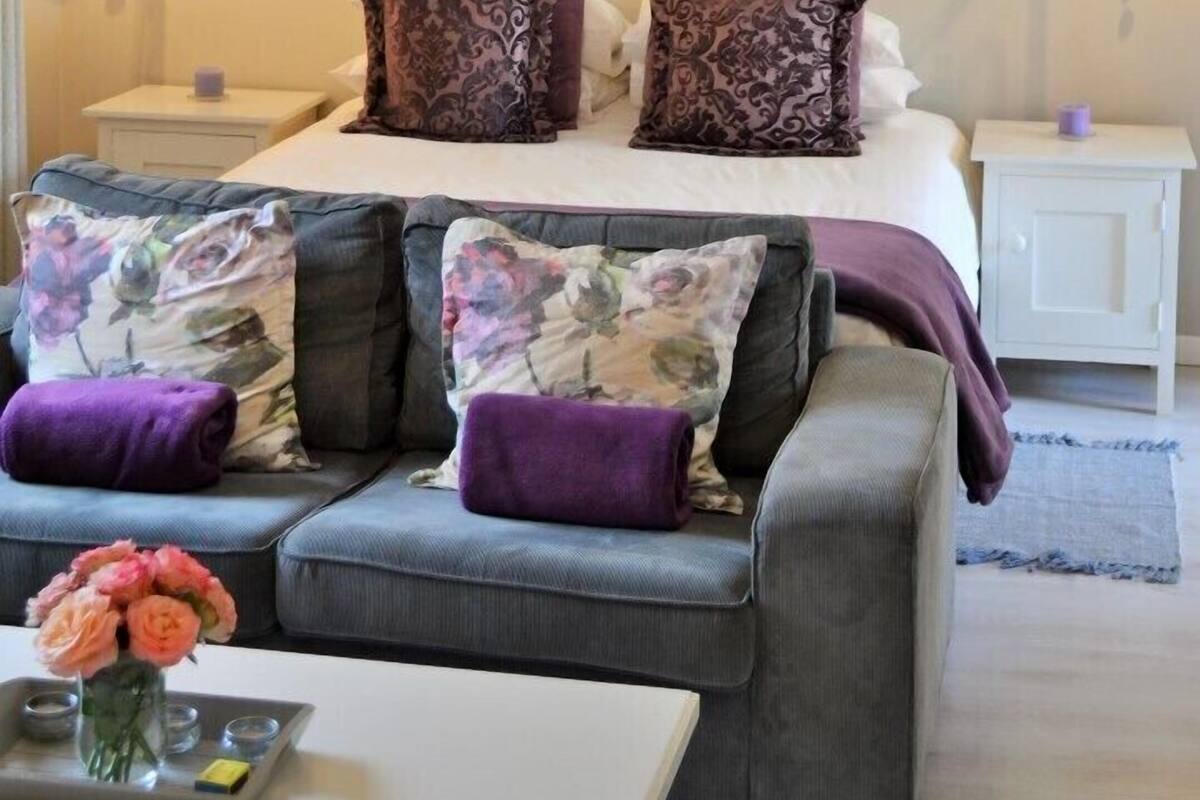 A bedroom with a bed, two nightstands, a chandelier, a sofa, and a painting on the wall.