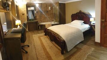 A hotel room with a large bed, a wooden desk with a lamp, a bathroom with a bathtub, and a mirror.