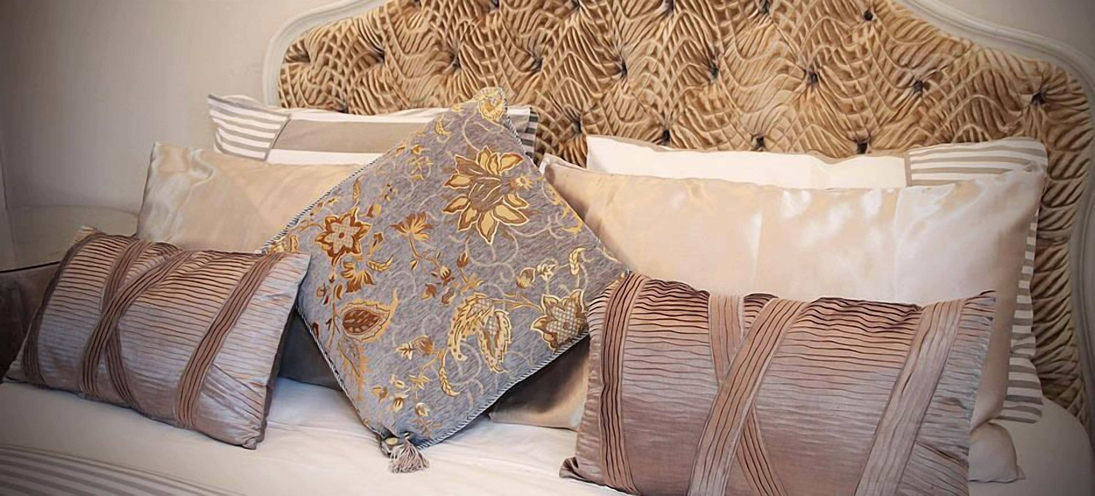 Una cama con cabecera capitonada, varios almohadones y una manta a rayas.