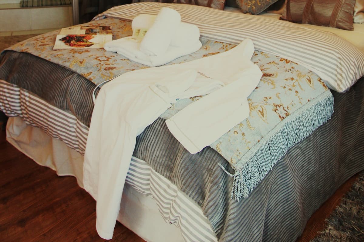 A hotel room with a large bed, a chandelier, a bathroom with a glass shower, and a mirror.