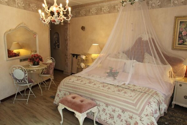 A bedroom with a canopy bed, a vanity with a mirror, a chair, and a bedside table with lamps.