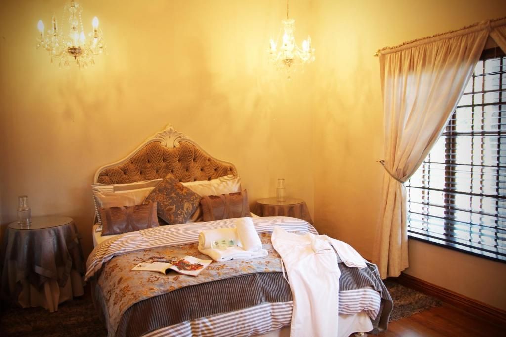 A bedroom with a large bed, two bedside tables, a chandelier, and a window with blinds.