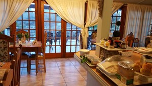 Un espace repas offrant une vue sur une terrasse extérieure enneigée, un buffet proposant divers plats et une table entourée de chaises.