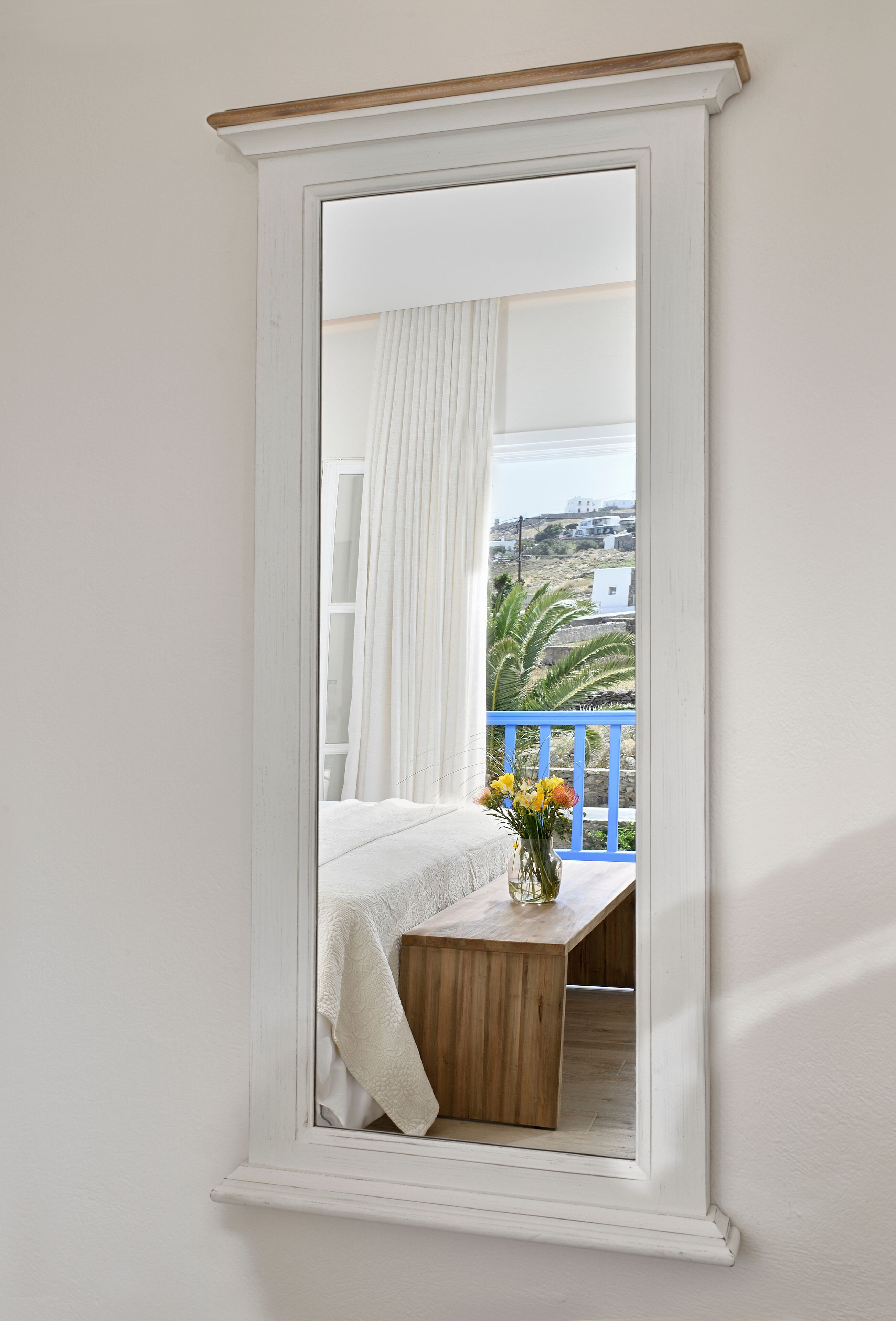 Un dormitorio con cama, mesita de noche de madera y ventana con vista a un balcón y edificios.