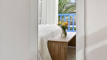 Un dormitorio con cama, mesita de noche de madera y ventana con vista a un balcón y edificios.
