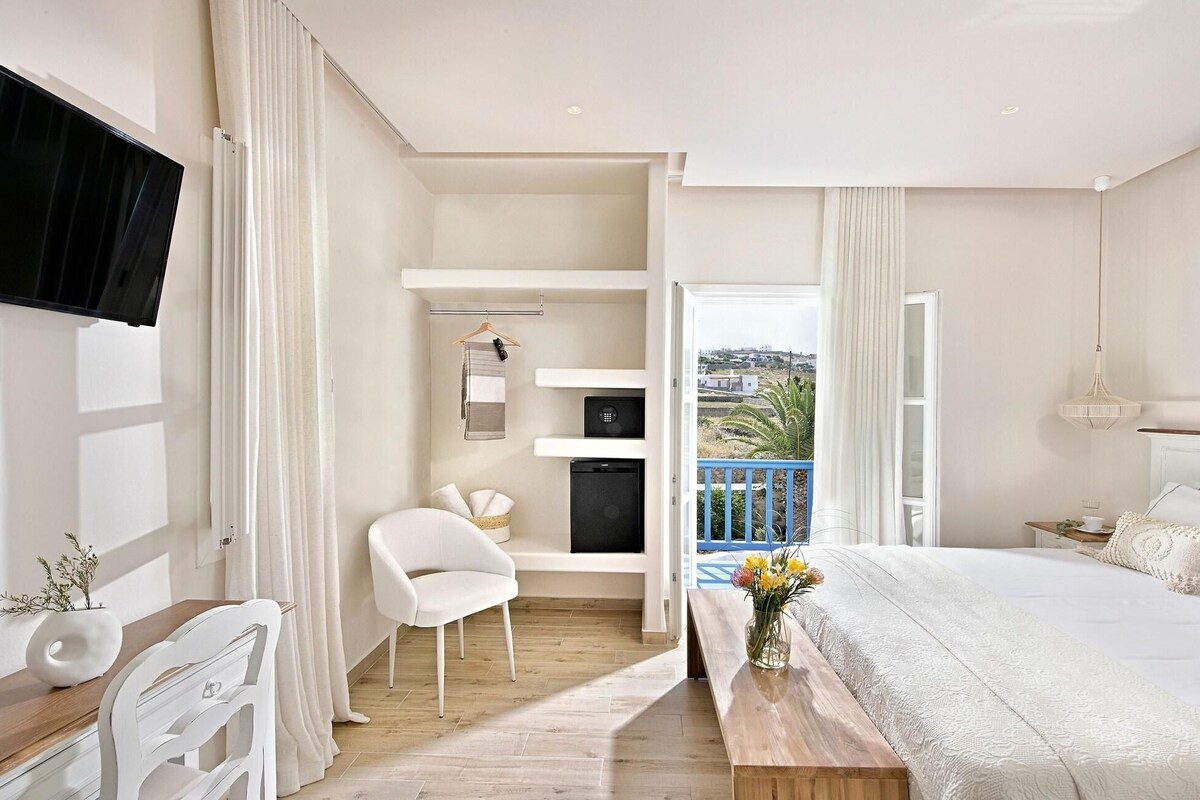 A modern bedroom with a bed, a desk, a chair, a TV, and a balcony with a view.