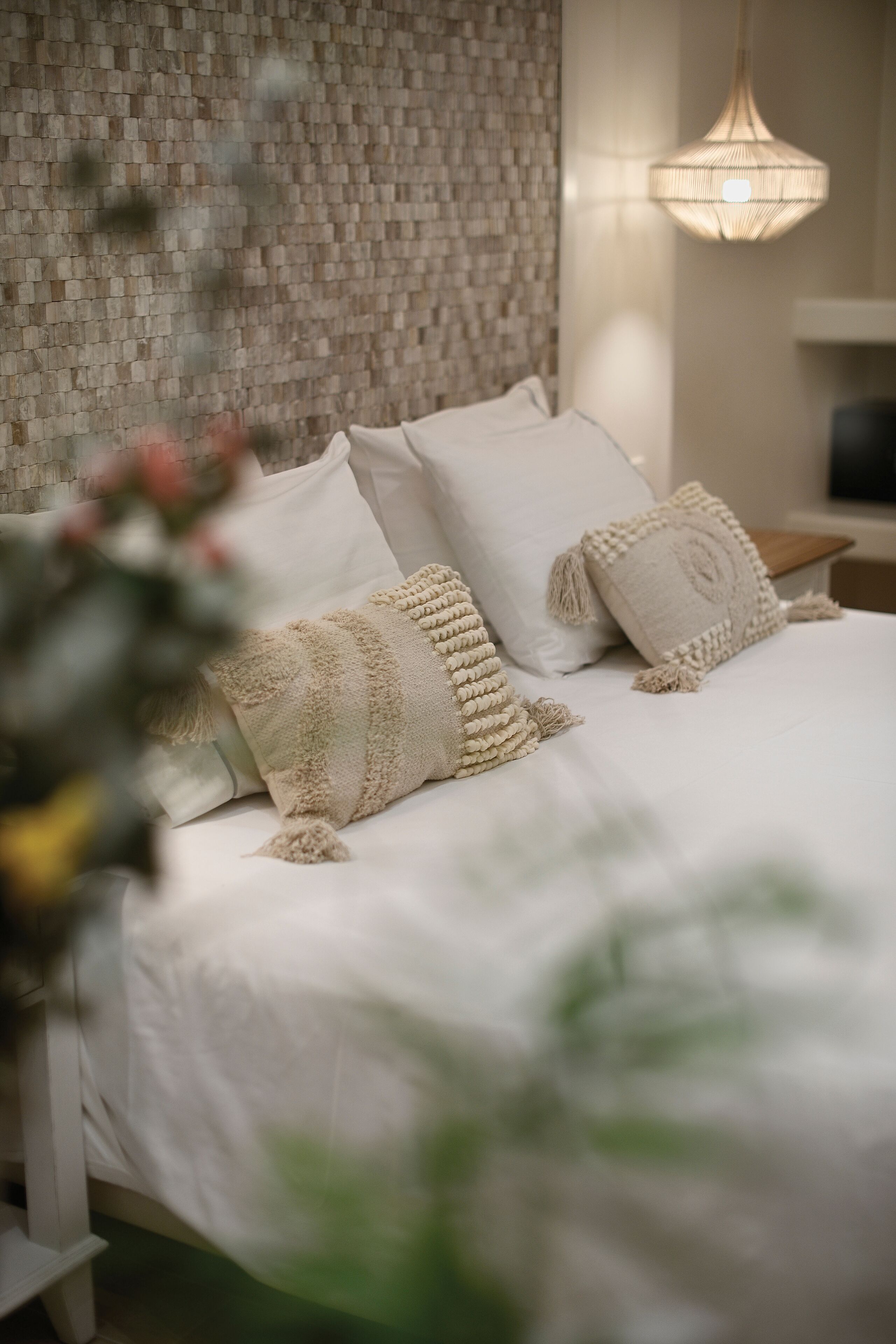 Una cama bien hecha con ropa blanca y almohadas decorativas, un cabecero tejido y una lámpara colgante.