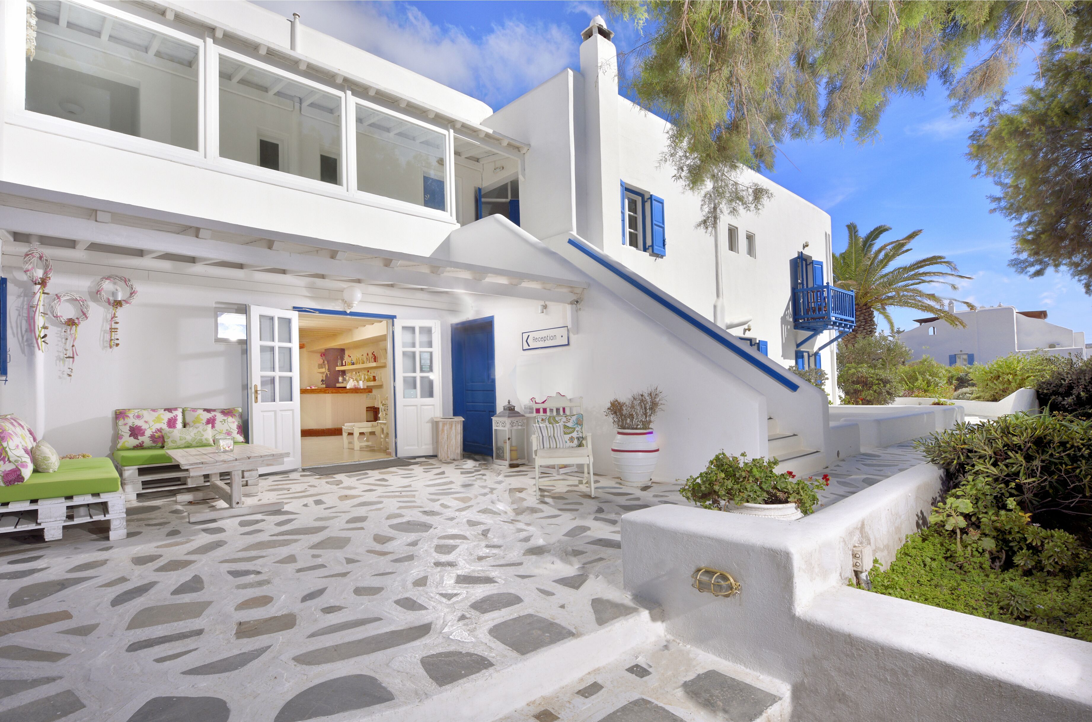 Un edificio blanco con un patio empedrado de piedra, una puerta azul y una escalera que sube al piso superior.