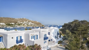 Un pueblo costero con edificios blancos y contraventanas azules, un puerto deportivo con barcos y una colina al fondo.