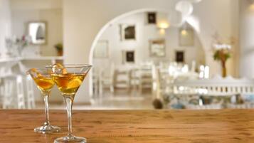 Deux verres à martini, décorés de tranches d’orange, sont posés sur une table en bois dans une pièce bien éclairée, où l’on trouve des meubles blancs et un arc décoratif également blanc.