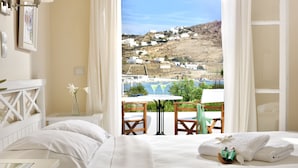 Habitación de hotel con cama, una mesa con sillas, vistas a un pueblo en la ladera y un balcón con mesa y sillas.