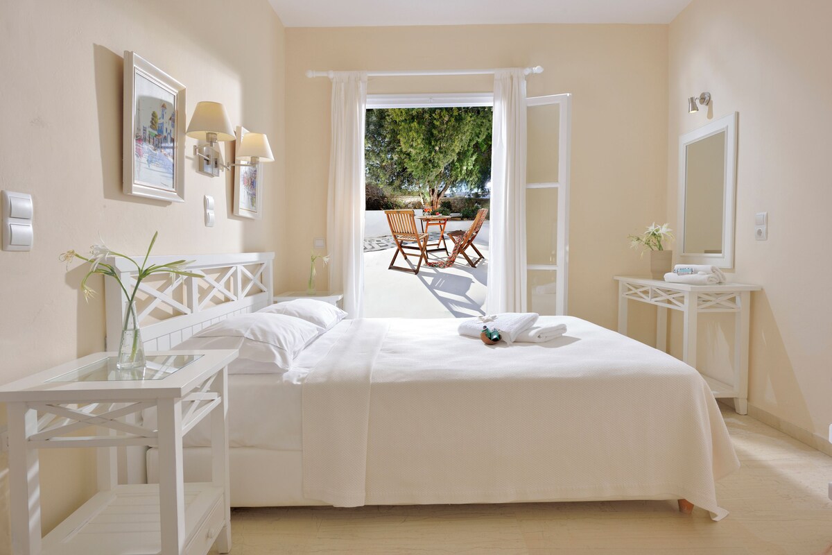 A bedroom with a bed, a bedside table, a chair, a small table, and a window with curtains.