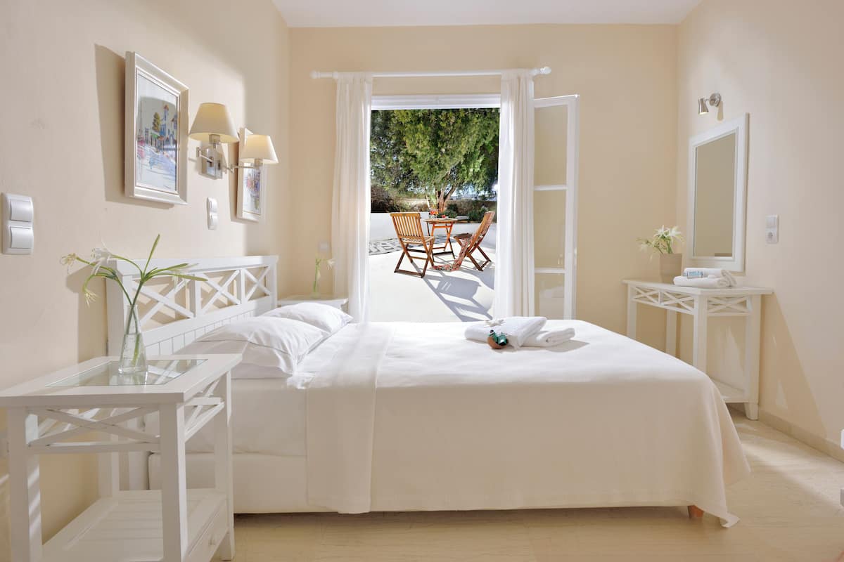 A bedroom with a bed, a bedside table, a chair, a small table, and a window with curtains.