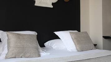 Un lit bien fait, avec des oreillers blancs et beiges, une tête de lit blanche et un miroir mural encadré de doré.