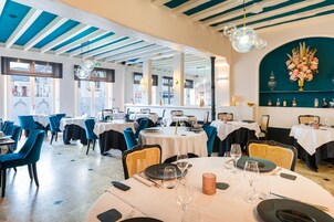 Un restaurant avec des tables rondes, des chaises bleues et un mur d’accent de couleur turquoise.