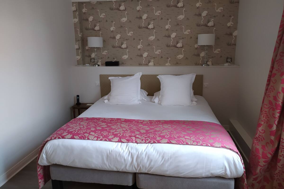 A hotel room with a bed, two bedside lamps, a nightstand, and a patterned wallpaper.