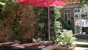 An outdoor patio with a table and chairs, a red umbrella, and a stone wall. -  Logis Hôtel Restaurant Le Cheval Blanc (Blere)