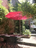Une terrasse extérieure avec une table et des chaises, un parasol rouge et un mur en pierre.