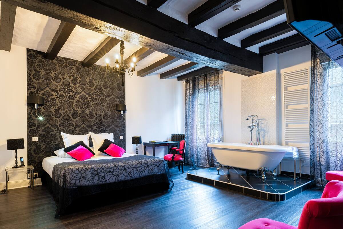 A modern bedroom with a large bed, a bathtub, and a desk.