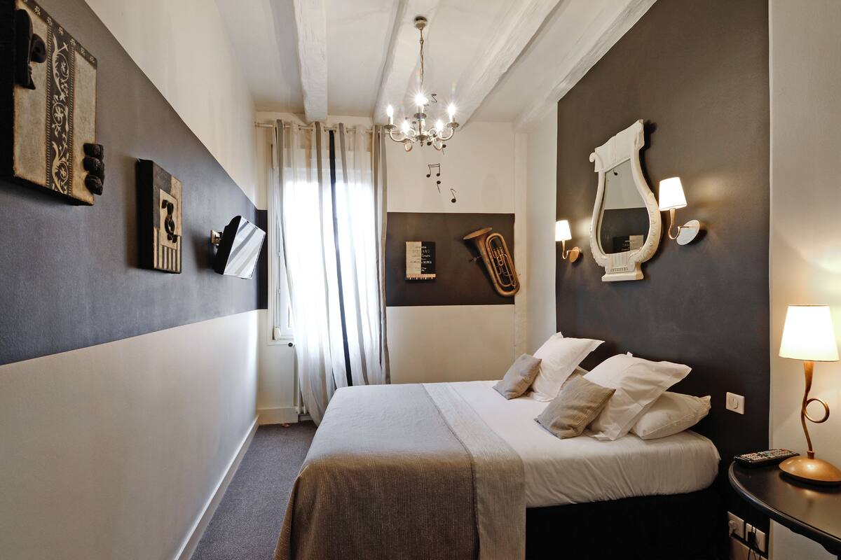 A hotel room with a bed, a chandelier, a mirror, and wall-mounted artwork.