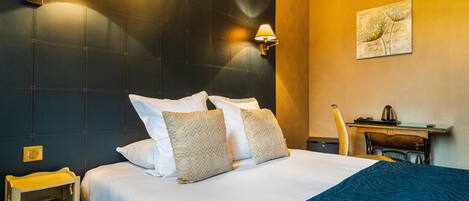 A hotel room with a large bed, two wall-mounted lamps, a desk with a chair, and a painting on the wall.