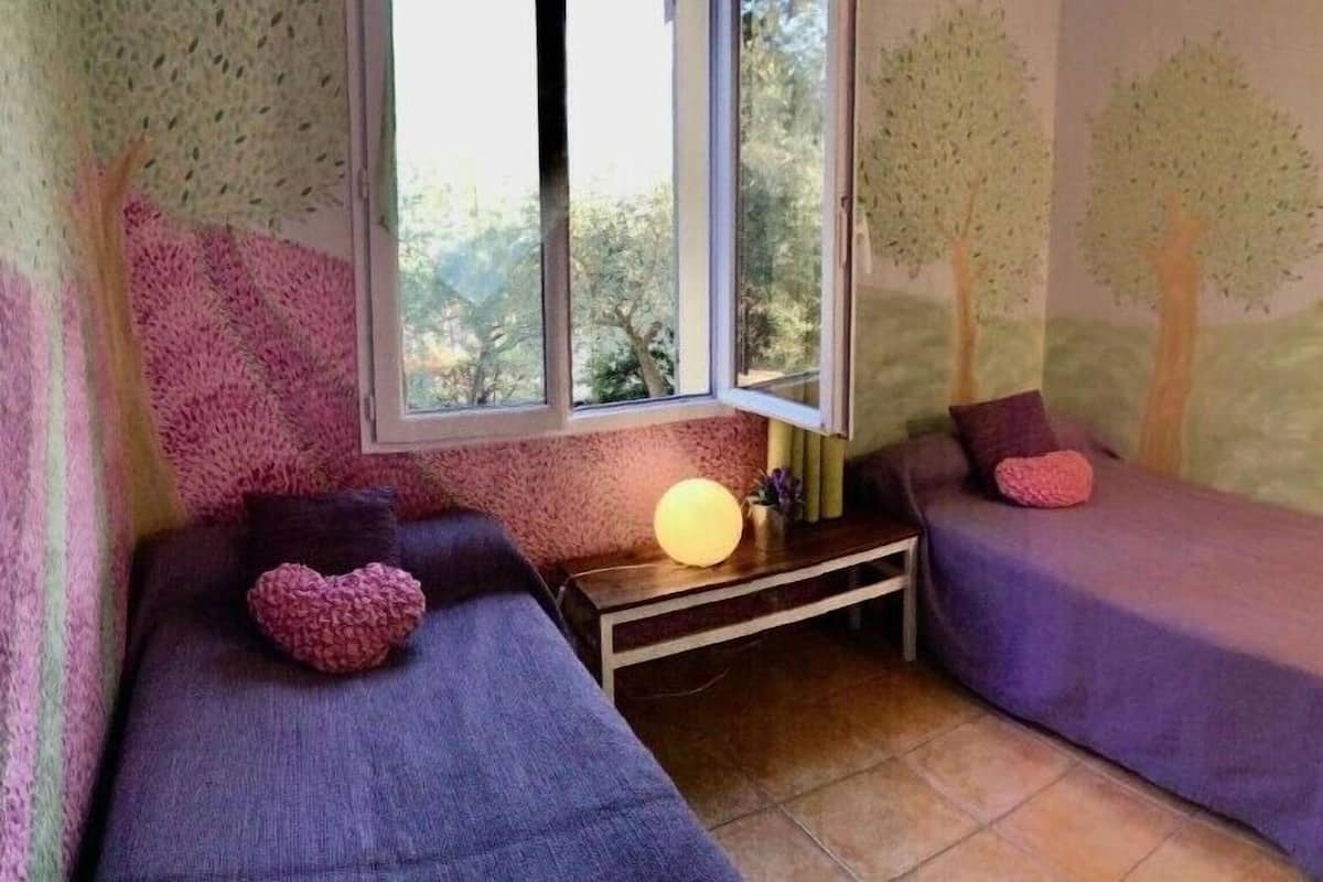 A room with two beds, a window, a lamp, and a mural on the wall.