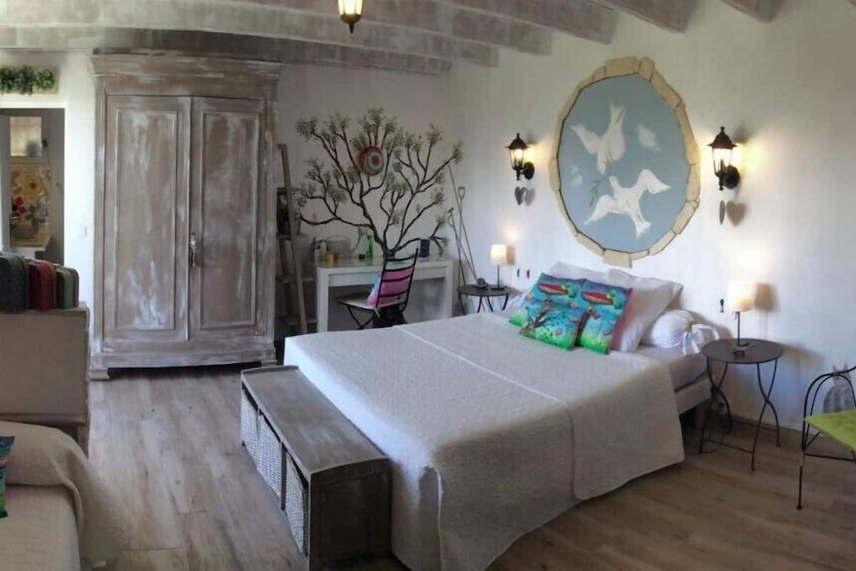 A bedroom with a large bed, a wardrobe, a desk, and wall-mounted lights.