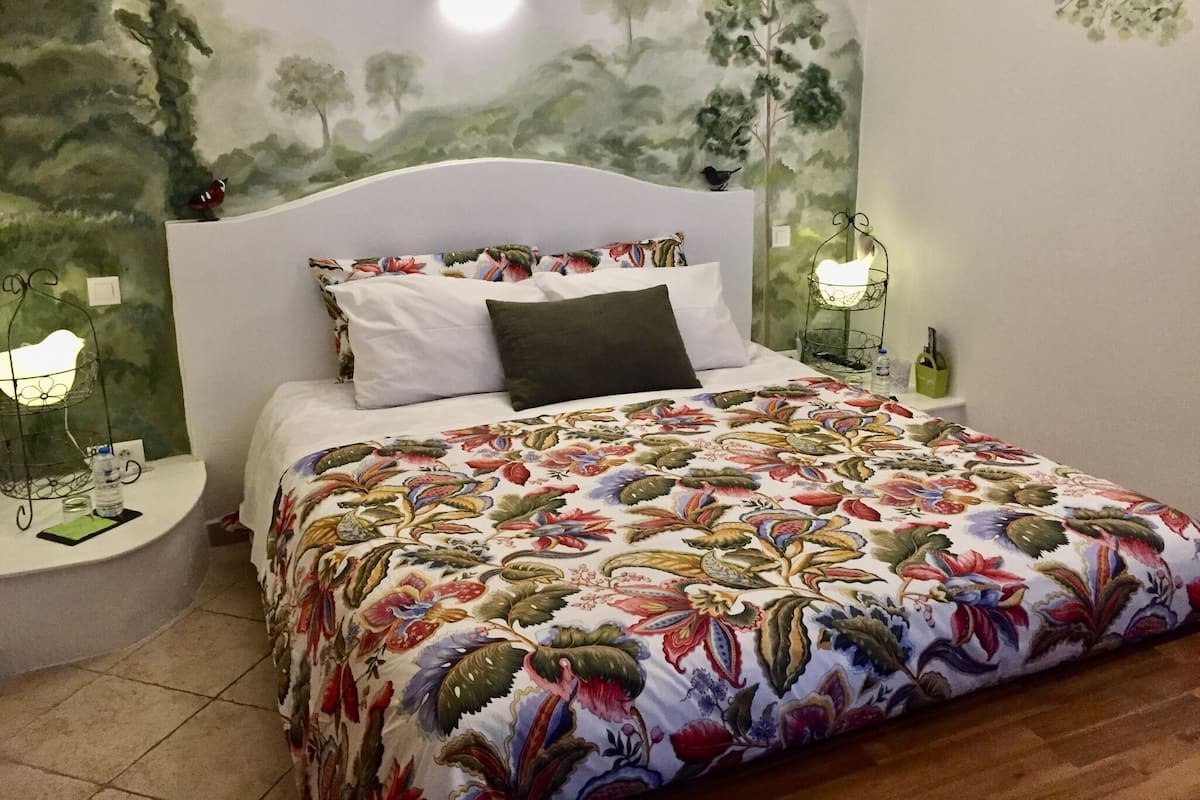 A neatly made bed with a floral bedspread, a white headboard, and a wall mural of trees.