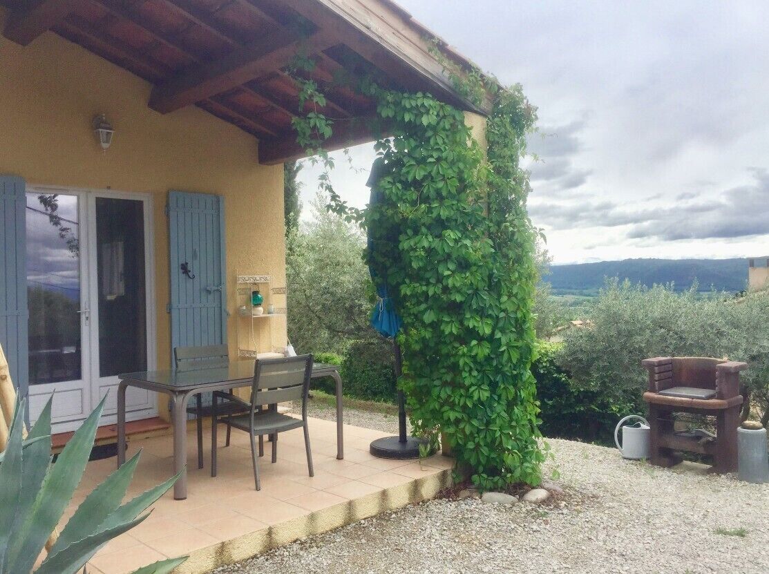 A covered patio with a table and chairs, a stone bench, and a wall covered in ivy.