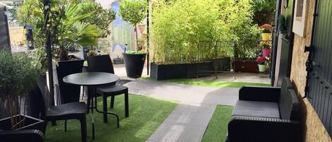 Un patio con mesa y sillas, rodeado de plantas en macetas y una cerca de bambú.