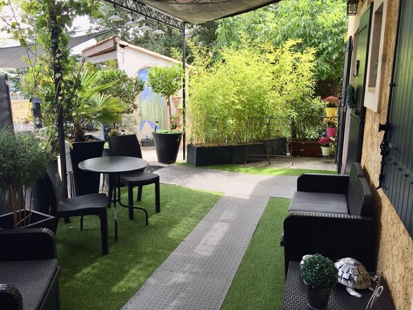 A patio area with a table and chairs, surrounded by potted plants and a bamboo fence. - Le Mas du Cadranier (Villeneuve)
