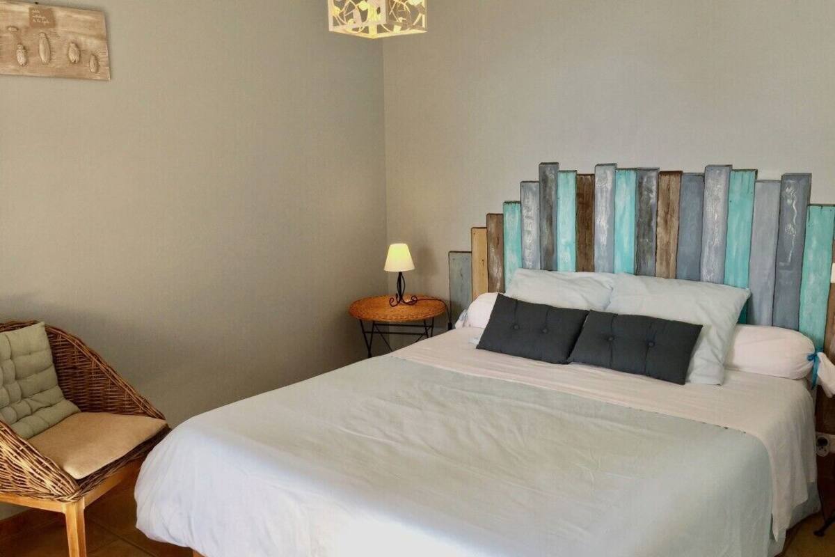 A bedroom with a bed, a chair, a nightstand, and a wall-mounted light fixture.