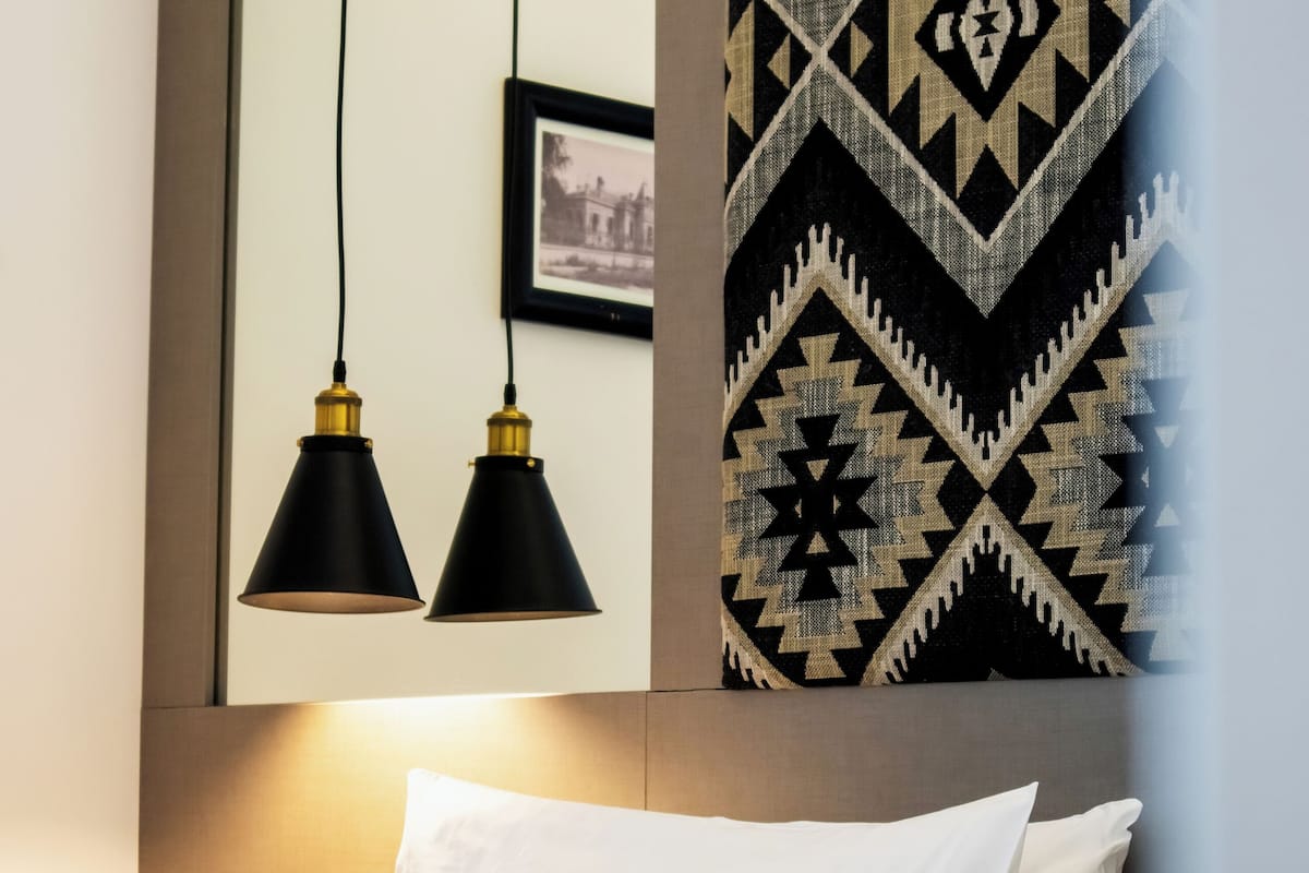 Un lit bien fait, agrémenté d’oreillers blancs et à motifs, une décoration murale en noir et blanc, et deux lampes suspendues noires.