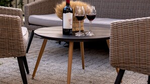 A wicker sofa and chairs around a round table with a bottle and glasses of red wine. - Thomas Albert Hotel (Chisinau)