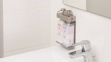 Une salle de bain avec des toilettes fixées au mur, un lavabo avec un robinet chromé et un miroir.