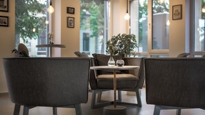 A modern interior with two grey upholstered chairs around a small round table, a potted plant, and a window with a view of greenery outside. - Thomas Albert Hotel (Chisinau)