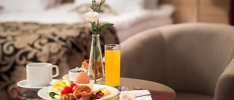 A breakfast setup with a glass table, a white cup, a plate of food, a glass of orange juice, and a vase with a white flower.