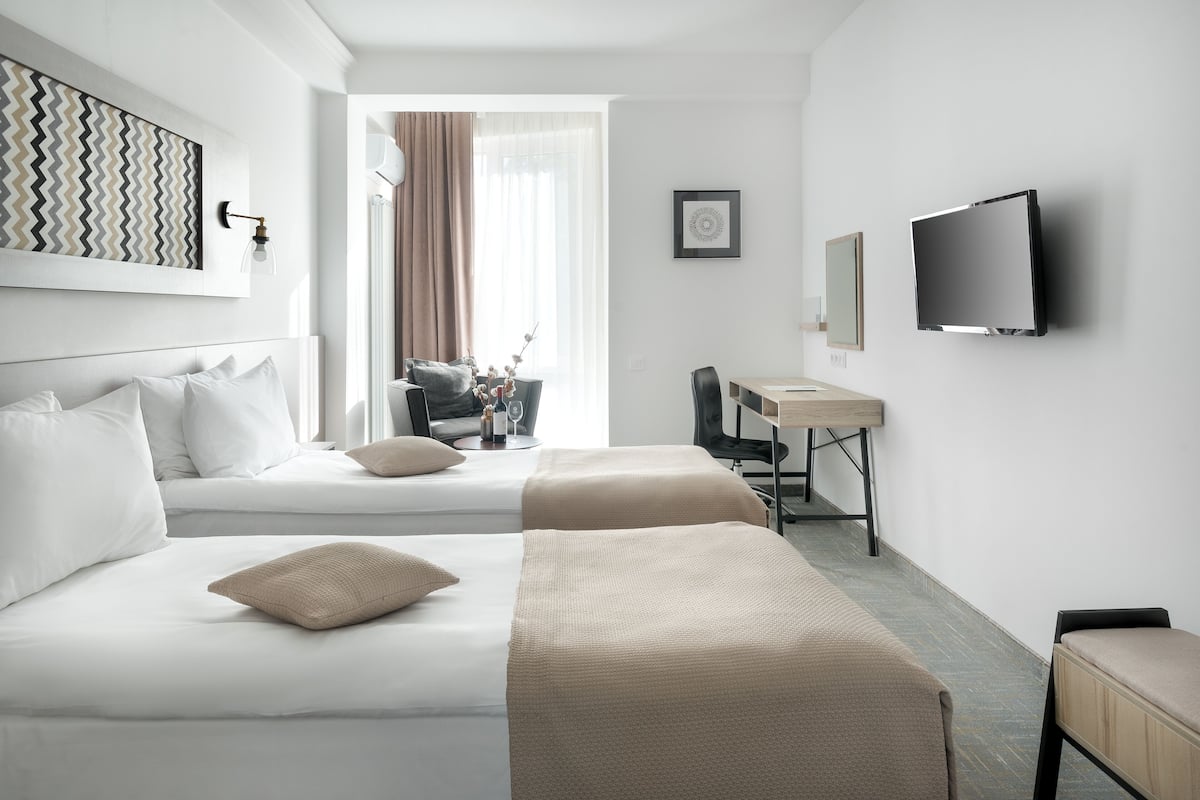 Une chambre d’hôtel avec deux lits, un bureau, une chaise, une télévision et une fenêtre avec des rideaux.