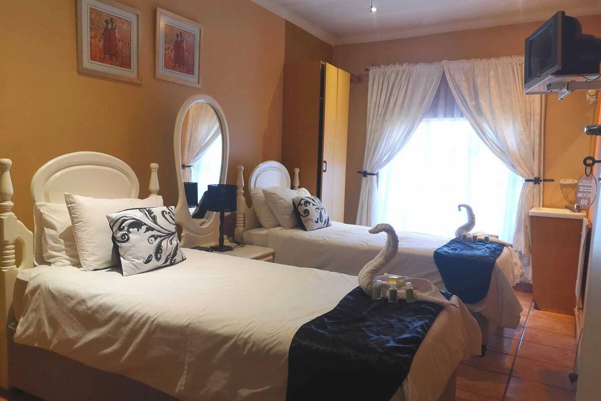 A hotel room with two beds, a TV mounted on the wall, a mirror, and a window with curtains.